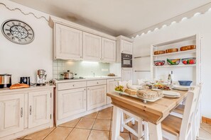 A kitchen with white cabinets, a wooden table set for dining, and a clock on the wall.