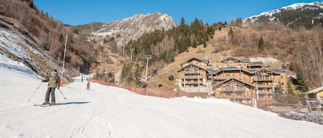 A ski resort with wooden lodges, a ski slope, and a mountain backdrop.