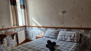 A bedroom with a checkered bedspread, a bedside table, a radiator, and patterned wallpaper. - Pine Lodge Hotel (Blackpool)