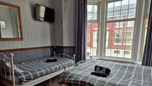 A room with two single beds, a TV mounted on the wall, and a window with a view of buildings outside. - Pine Lodge Hotel (Blackpool)