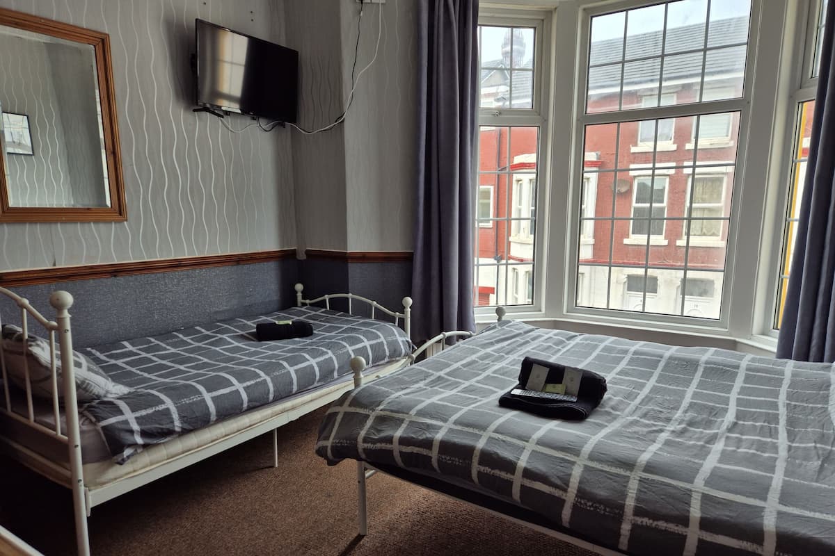 Habitación con dos camas individuales, un televisor montado en la pared y una ventana con vistas a edificios.