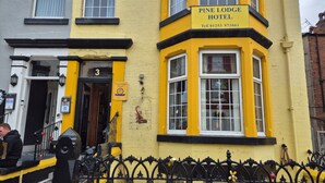 The exterior of Pine Lodge Hotel with a yellow facade, black trim, and a black wrought iron fence. - Pine Lodge Hotel (Blackpool)