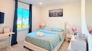 Un dormitorio con cama, escritorio, mesita de noche, espejo y ventana con cortinas.