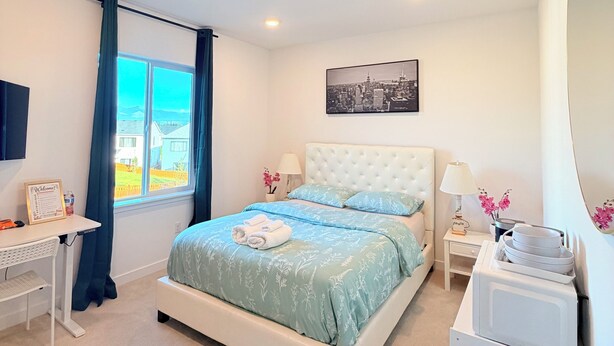 Un dormitorio con cama, escritorio, mesita de noche, espejo y ventana con cortinas.