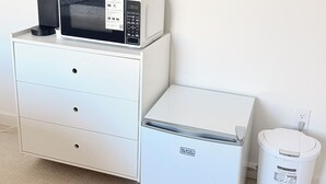 Una kitchenette con cafetera, microondas, refrigerador y un cesto de basura.