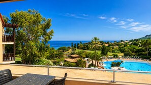 A poolside view with a clear view of the ocean, a pool, and surrounding greenery.
