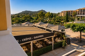 A rooftop restaurant with outdoor seating, a sign reading 'CRÈPES - GAUFRES,' and a view of a hilly landscape with buildings in the background.