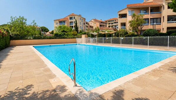 A swimming pool with a metal ladder, surrounded by a tiled deck, and adjacent to multi-story buildings with balconies. - Fréjusienne getaway (Fréjus)