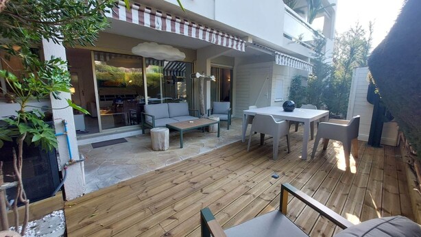 Une terrasse avec des meubles d’extérieur, un sol en pierre et une vue sur l’intérieur à travers des portes vitrées.