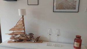 Une console blanche ornée d’une sculpture en bois décorative, de deux photophores en verre et d’un pot à bougie rouge.