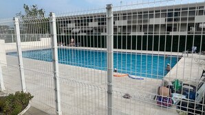 Une piscine entourée d’une clôture, avec un bâtiment visible à l’arrière-plan.