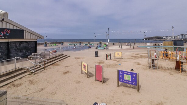 Une plage avec une promenade en bord de mer, un restaurant appelé « Gyro » et un panneau indiquant un jeu dont le thème est celui d’une paire.