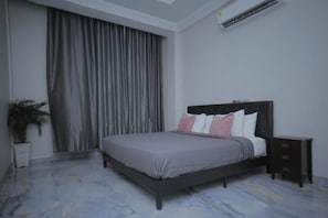 Un dormitorio con una cama, una mesita de noche, una planta en maceta y un ventanal con cortinas.