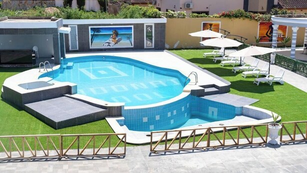 En swimmingpool med et unikt, buet design, omgivet af en velholdt græsplæne og liggestole.