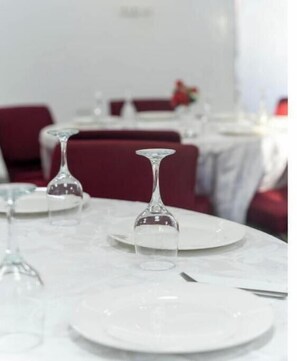 A dining table with white plates and clear wine glasses, set for a meal. - Adonai 1-bedroom apartment unit #6 (Spintex)