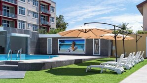Une piscine ornée d’une fresque murale, avec des chaises longues et un bâtiment en arrière-plan.
