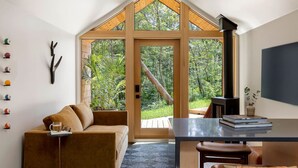 A cozy room with a large window, a wooden ceiling, a brown sofa, a small table, and a TV. - Modern+Hot Tub+Hocking Hills+ Near Waterfalls (Logan)