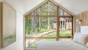 A bedroom with a large window overlooking a forested area and a wooden staircase. - Modern+Hocking Hills+Hot Tub+Near Waterfalls (Logan)