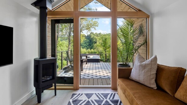 A modern interior with a large wooden-framed window, a black fireplace, and a cozy seating area with a patterned rug. - Modern+Hocking Hills+Hot Tub+Near Waterfalls (Logan)