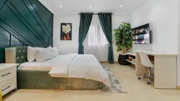 A modern bedroom with a bed, a desk, and a TV. - Rext  Apartment  (Abuja)
