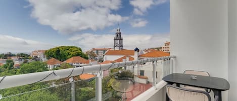 A balcony with a table and chairs, overlooking a cityscape with buildings and a clock tower.