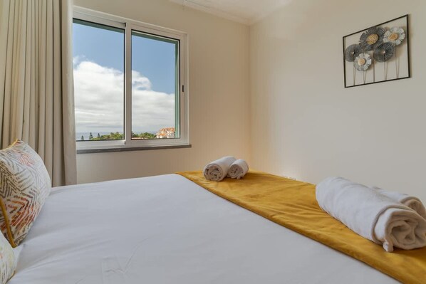 Une chambre d’hôtel avec un grand lit, une fenêtre donnant sur un beau paysage et une œuvre d’art murale.