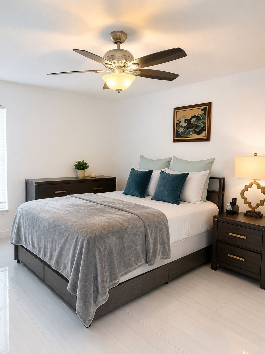 A bedroom with a bed, nightstands, a ceiling fan, a bedside lamp, and a wall-mounted artwork.