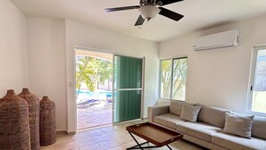 A living room with a sofa, a coffee table, a ceiling fan, and a view of the outside.