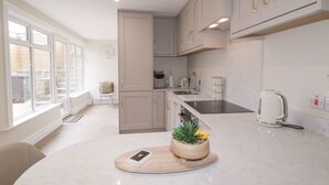 A modern kitchen with white cabinets, a built-in oven, a sink, and a kettle. There is a window providing natural light and a plant on the countertop. - 41 Church View (Portstewart)