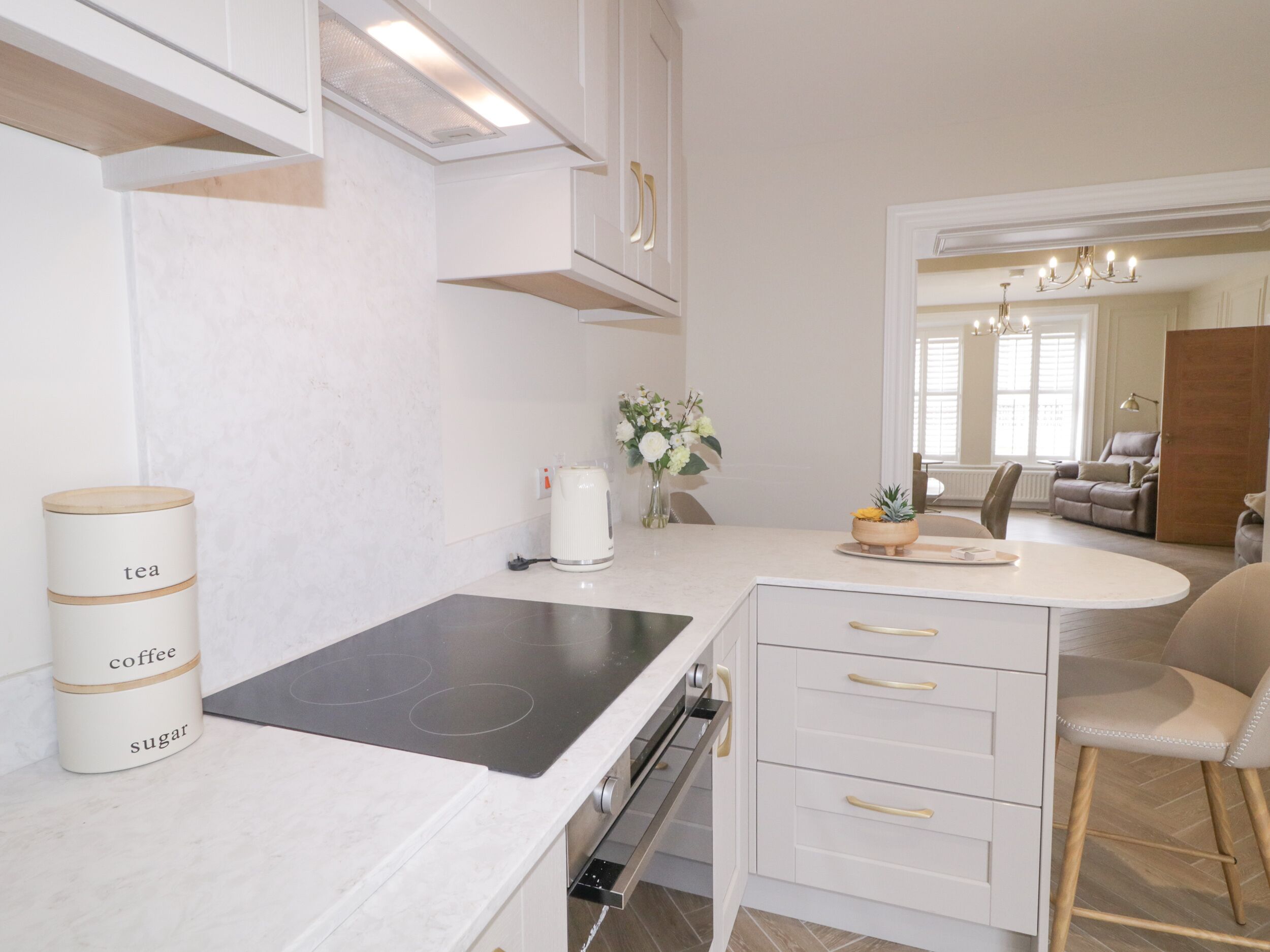 A modern kitchen with a built-in stove, white cabinetry, and a coffee station.