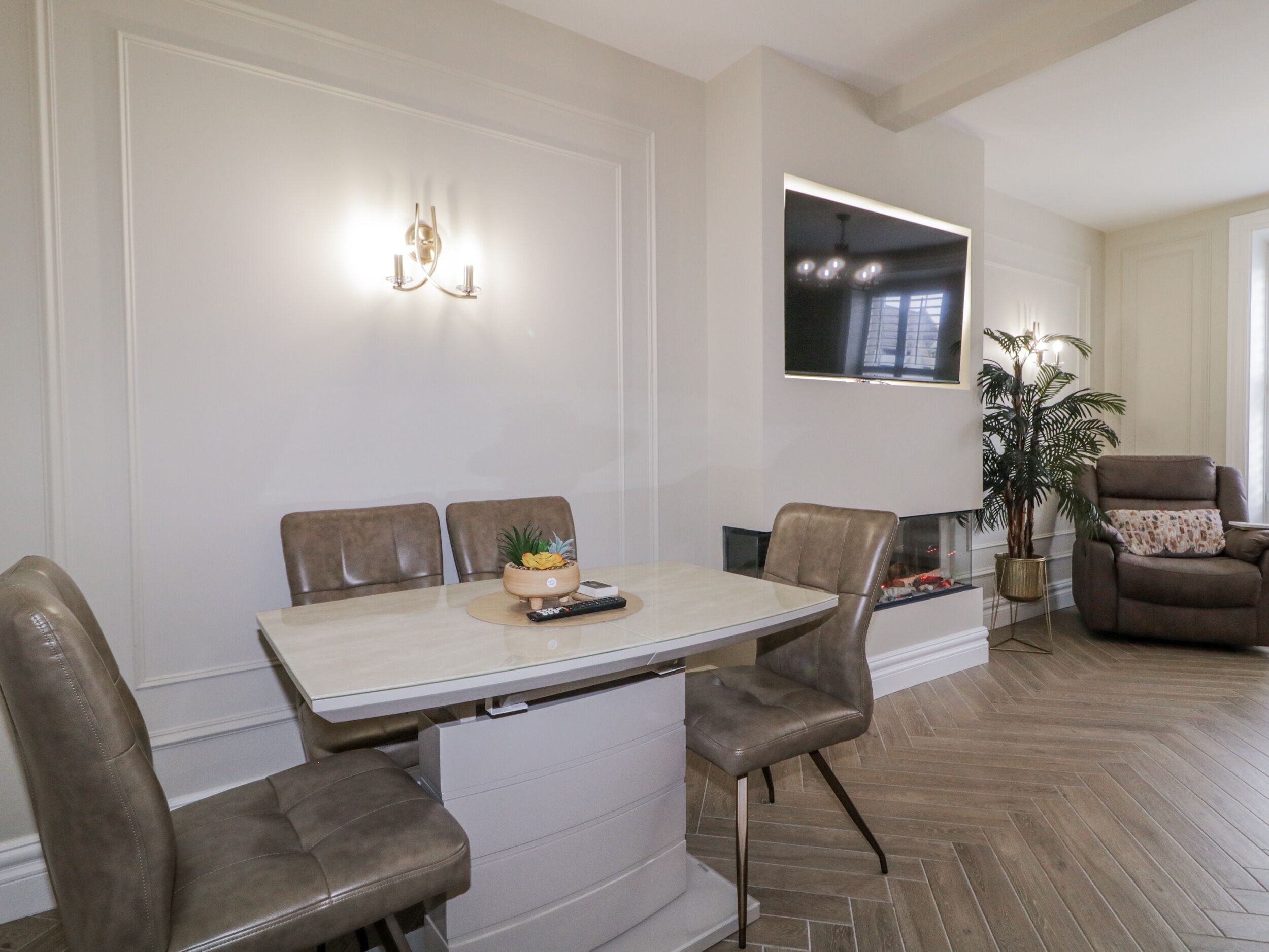 A dining area with a table, chairs, a remote control, and a small plant on the table.