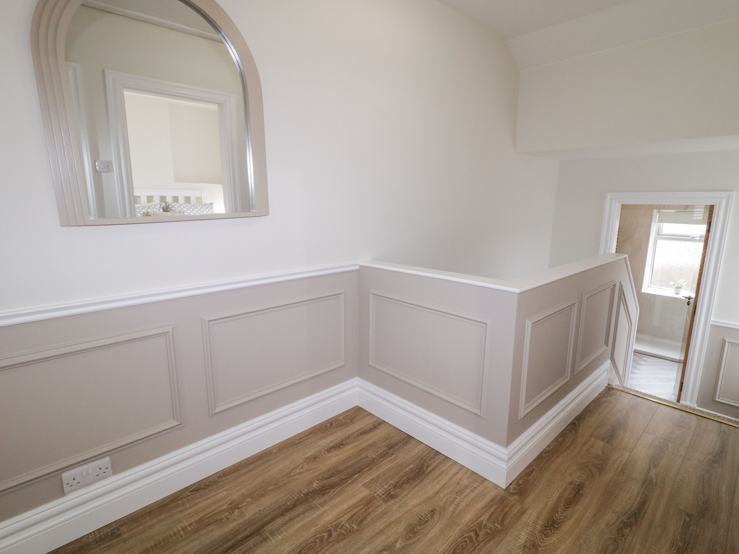 A room with a wooden floor, white walls, and a large mirror.