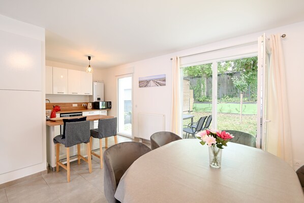 A modern kitchen with white cabinets, a red kettle, and a dining area with a table and chairs.