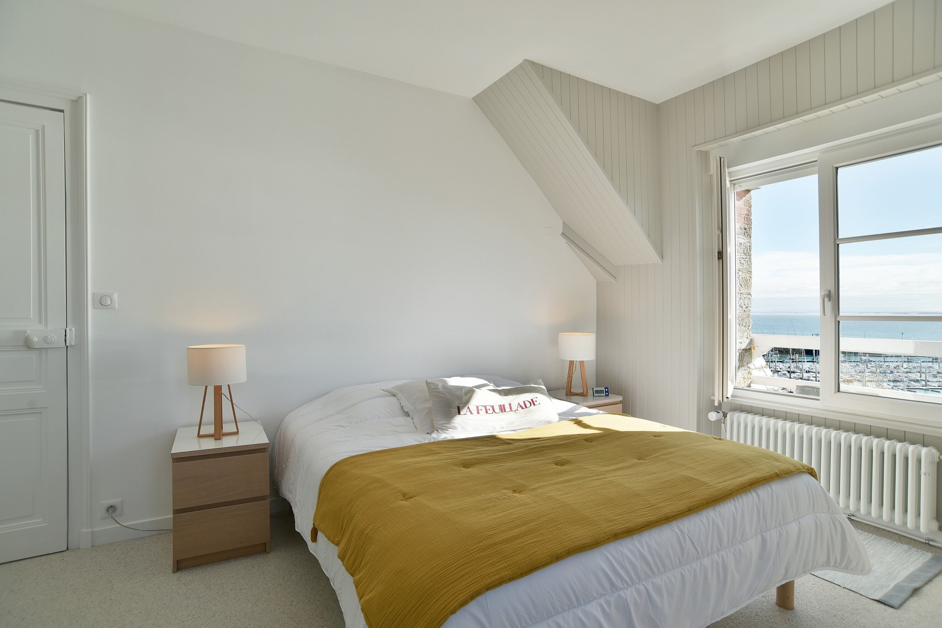 Une chambre à coucher comprenant un lit, des tables de chevet, une lampe, une fenêtre avec vue et une étagère fixée au mur.