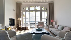 Una sala de estar moderna con un sofá, sillones, una mesa de centro y un televisor. Amplias ventanas ofrecen vistas al exterior.