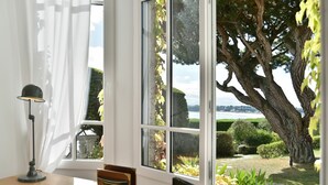 Una habitación con un escritorio, una lámpara y un amplio ventanal con vista a un árbol y un jardín.