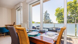 A dining area with a wooden table set for four, wicker chairs, and a view of the city through large windows. - An Ti Gwerned - Proche Aéroport Rennes (Saint-Jacques-de-la-Lande)