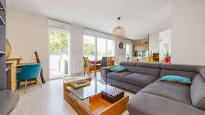 A modern living room with a grey sofa, a glass coffee table, and a dining area with a wooden table and chairs. - An Ti Gwerned - Proche Aéroport Rennes (Saint-Jacques-de-la-Lande)
