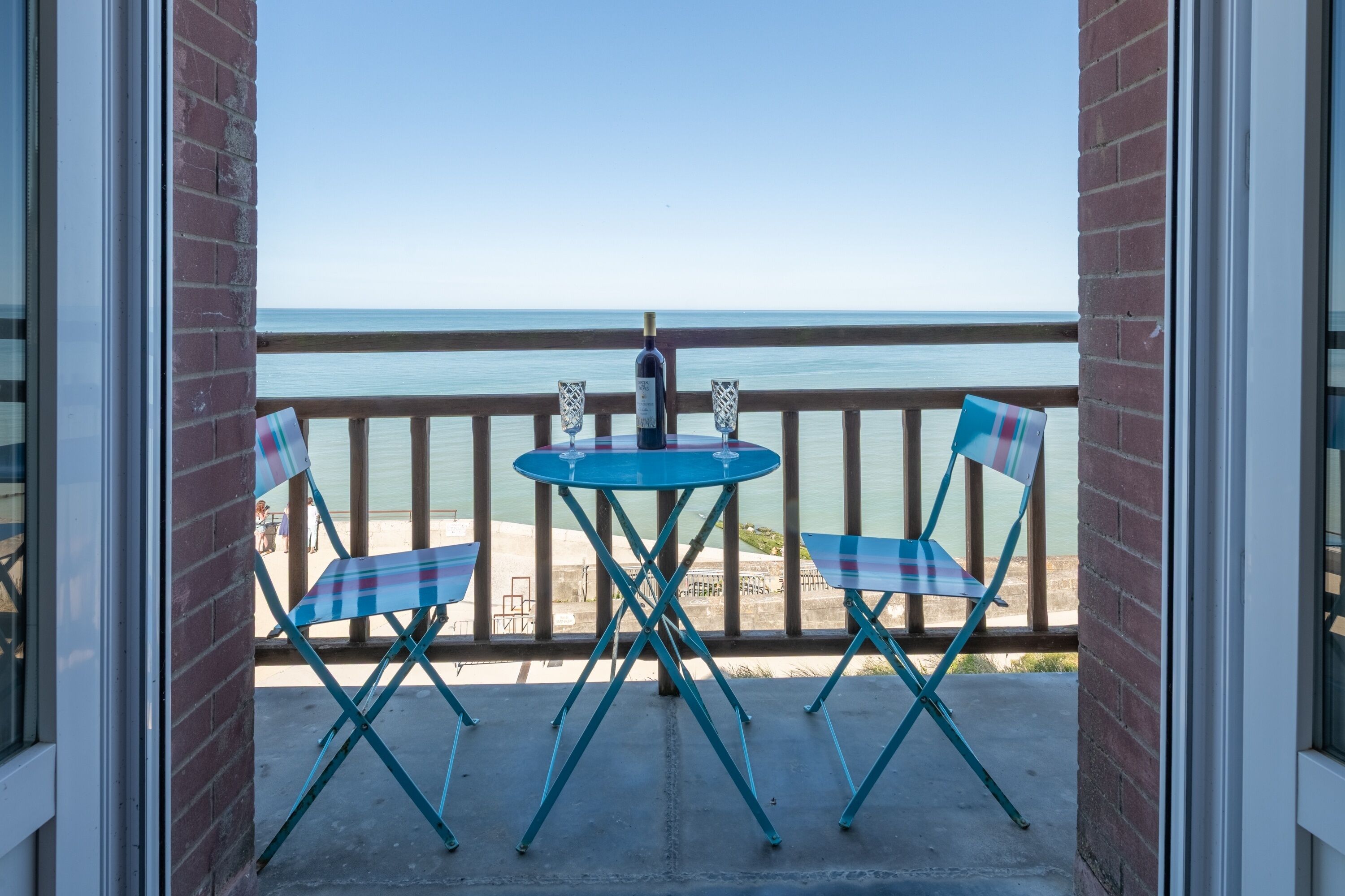 A balcony with a table and chairs, a bottle of wine, and a view of the sea.