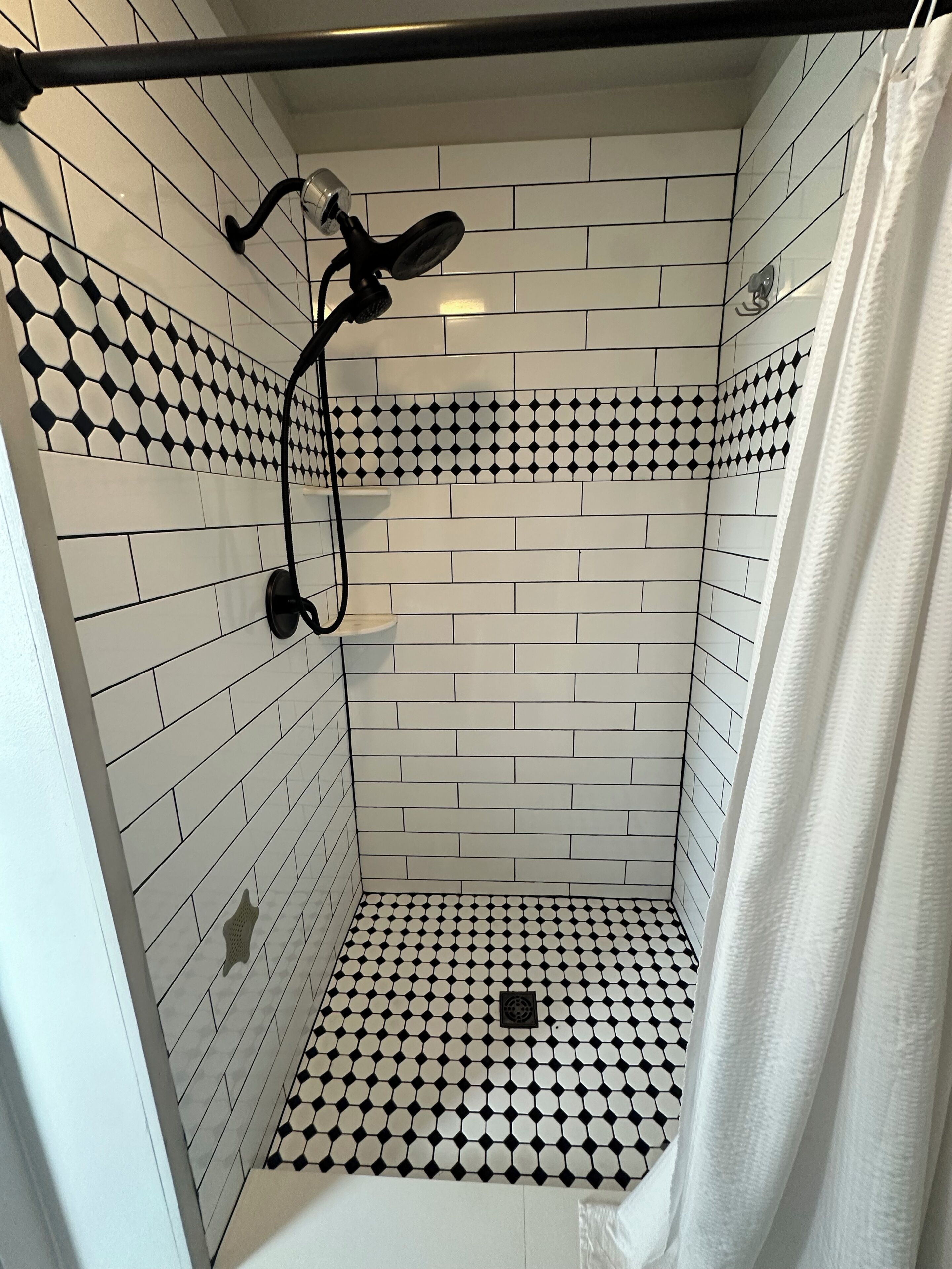 Eine Dusche mit einem schwarz-weiß karierten Boden, einem weißen Duschvorhang und einem schwarzen Duschkopf.