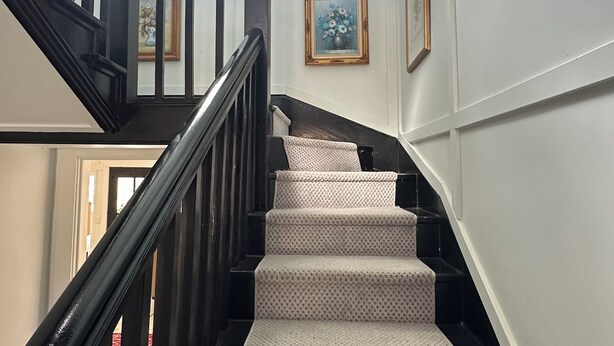 A staircase with a patterned carpet, wooden handrail, and framed artwork on the walls. - Charming Farmhouse, Peaceful and Private (Hurricane Mills)