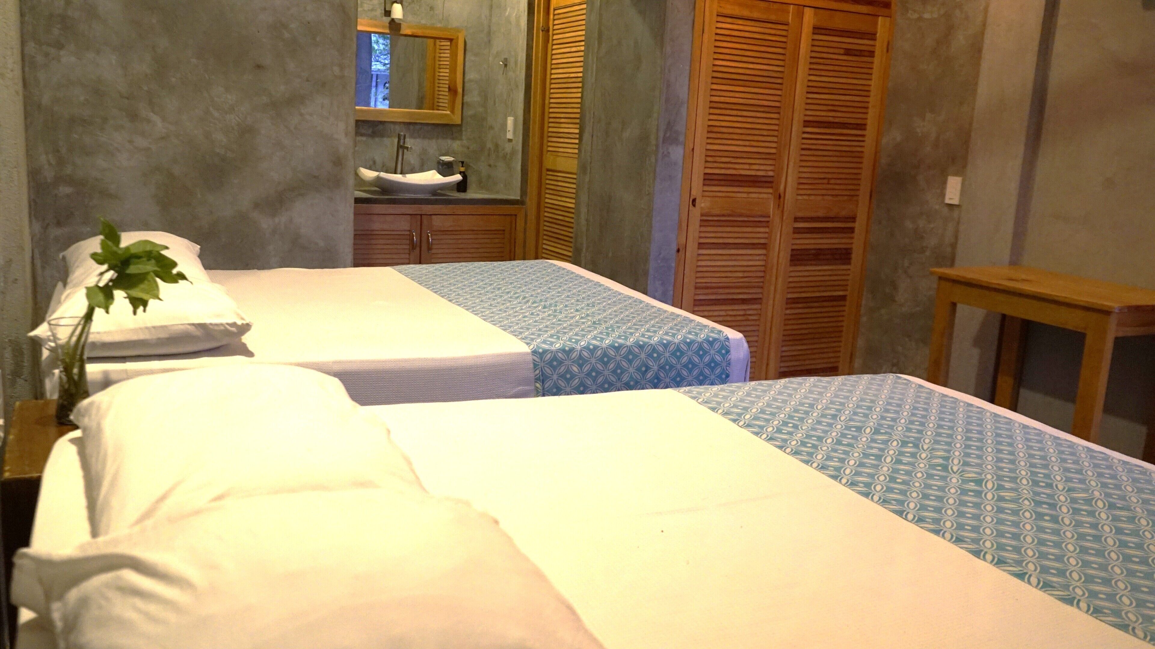 Ein Hotelzimmer mit zwei Betten, einem Holzschrank, einem kleinen Tisch und einem Spiegel.