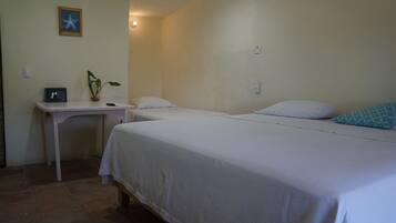A room with two beds, a small table with a plant, a framed picture, and a light switch on the wall.