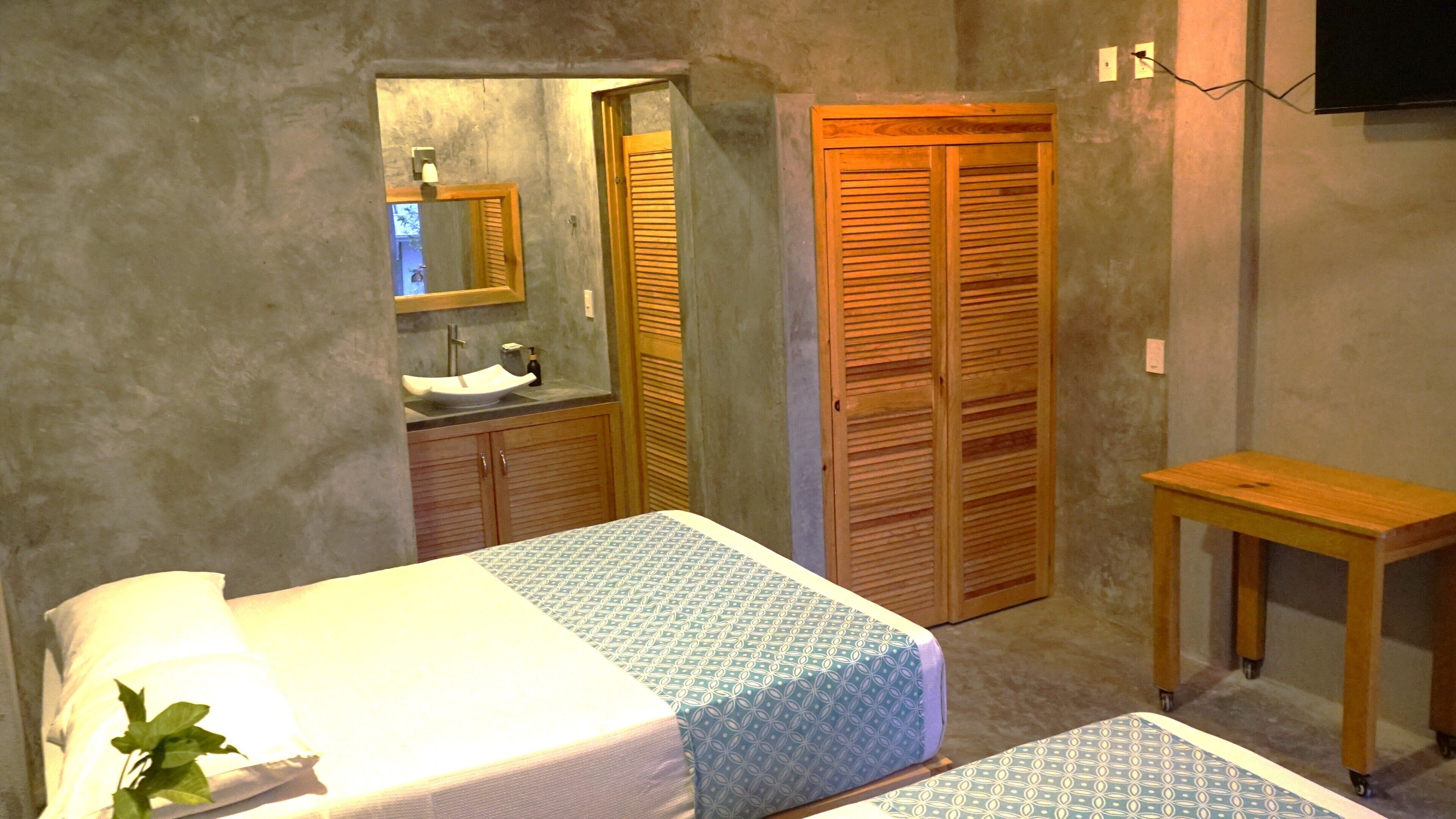 A bedroom with a bed, a bedside table, a mirror, a wooden wardrobe, and a bathroom with a sink.