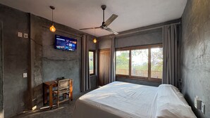 A bedroom with a bed, a desk, a ceiling fan, a TV mounted on the wall, and a window with curtains.