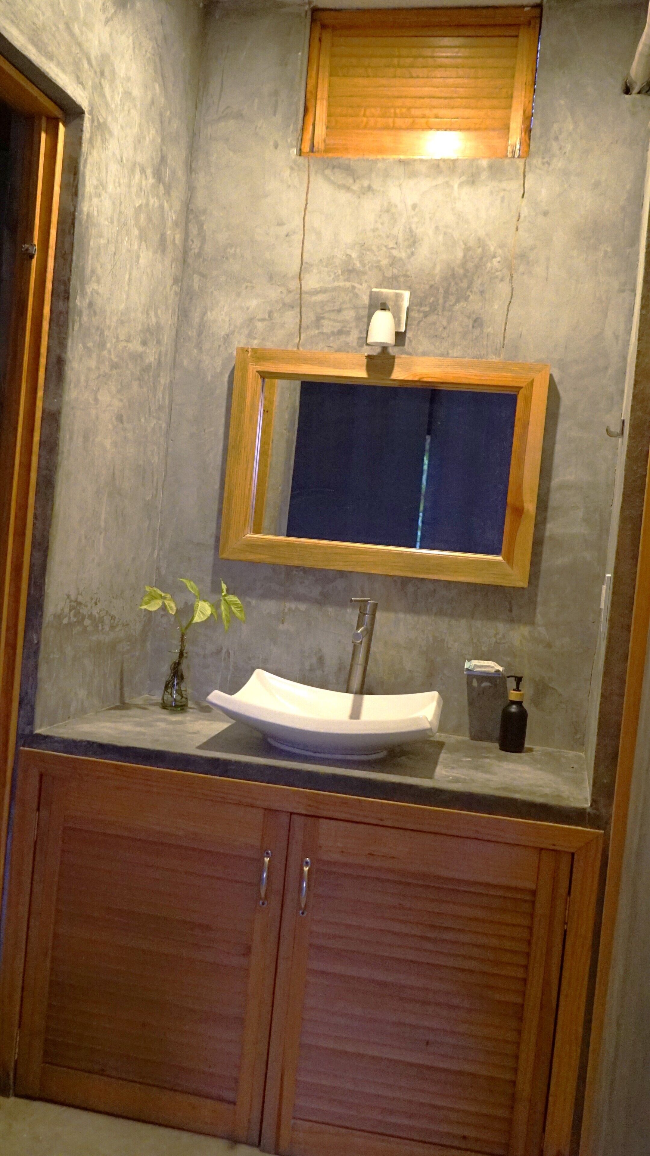 A bathroom with a wooden vanity, a vessel sink, a mirror, and a wall-mounted light fixture.