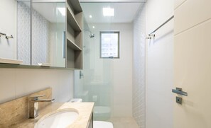 A modern bathroom with a glass-enclosed shower, a large mirror, and a beige marble countertop.