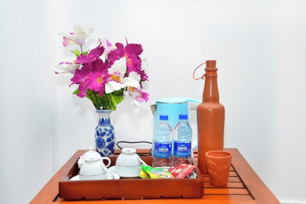 A tray with a vase of flowers, two water bottles, a teapot, a cup, and a small packet.