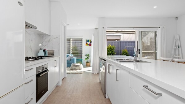 A modern kitchen with white cabinetry, a built-in oven, and a large island with a sink. - Serenity on Seaside - Kingscliff (Kingscliff)