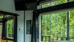 A bedroom with a bed, a window with a view of trees, a black curtain, and a mounted television. - Sasquatch soak shack (Mena)